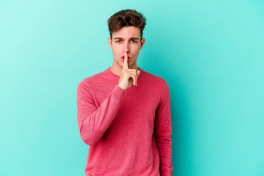Mavi arka planda izole edilmiş genç beyaz bir adam ya sır saklıyor ya da sessizlik istiyor..