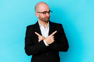 Mavi arka plan noktalarında izole genç beyaz adam iki seçenek arasında seçim yapmaya çalışıyor..