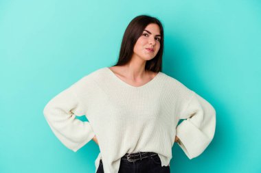 Kafkasyalı genç bir kadın mavi arka planda izole edilmiş, kafası karışmış, şüpheli ve kendinden emin değil..