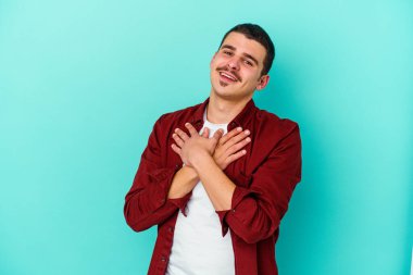 Mavi arka planda izole edilmiş beyaz bir genç, dost bir ifadeye sahip, avuçlarını göğsüne bastırıyor. Aşk konsepti.