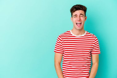 Kafkasyalı genç adam mavi arka planda izole edilmiş. Çok kızgın, öfkeli, hayal kırıklığına uğramış..