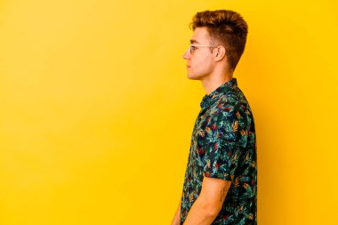 Hawaii tişörtü giyen genç beyaz adam sarı arka planda izole edilmiş, sola bakıyor, yandan poz veriyor..