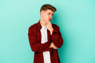 Kafkasyalı genç adam mavi arka planda izole edilmiş düşünüyor ve bakıyor, yansıtıyor, düşünüyor, bir fantezi kuruyor..