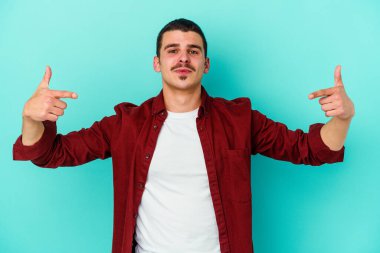 Kafkasyalı genç adam mavi arka planda izole edildi. Parmakları aşağıda, olumlu bir his var..