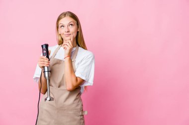 Genç Rus aşçı kadın, elinde elektrikli mikser tutarken, yanlamasına şüpheli ve şüpheci bir ifadeyle bakıyor..