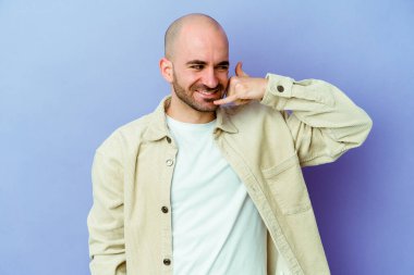 Mor arka planda izole genç beyaz adam parmakları ile bir cep telefonu çağrı jesti göstermektedir.