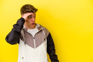 Kafkasyalı genç adam sarı arka planda izole edilmiş, uzaklara bakıyor ve elini alnına koyuyor..