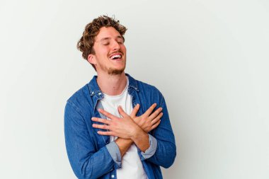 Beyaz arka planda soyutlanmış beyaz tenli genç bir adam gülüyor, elini yüreğine koyuyor, mutluluk kavramını koruyor..