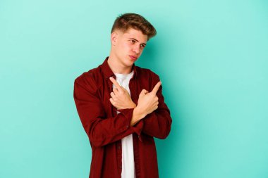 Mavi arka plan noktalarında izole genç beyaz adam, iki seçenek arasında seçim yapmaya çalışıyor.