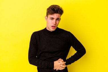 Sarı arka planda karaciğer ağrısı çeken, karnı ağrıyan genç beyaz bir adam..