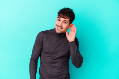 Mavi arka planda izole edilmiş genç beyaz adam bir dedikoduyu dinlemeye çalışıyor..