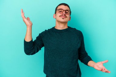 Kafkasyalı genç adam mavi arka planda izole edilmiş. Kafası karışmış ve omuz silkiyor. Kopya alanını tutmak için..