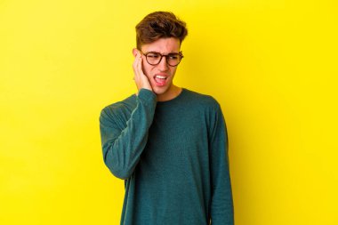 Sarı arka planda izole edilmiş genç beyaz adam elleriyle kulakları örtüyor..