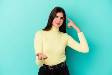 Beyaz bir kadın mavi arka planda izole edilmiş ve elinde bir ürün tutuyor..