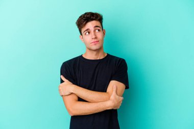 Kafkasyalı genç adam mavi arka planda izole edilmiş hedeflerine ve amaçlarına ulaşma hayali kuruyor.