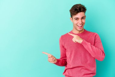 Mavi arka planda izole edilmiş genç beyaz adam işaret parmağıyla fotokopi alanını işaret ederek heyecan ve arzusunu ifade ediyor..