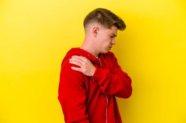 Sarı arka planda izole edilmiş, omuz ağrısı olan genç beyaz bir adam..