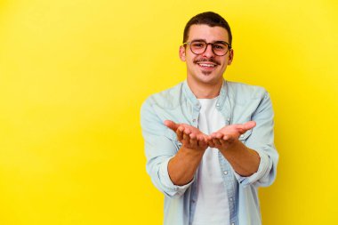 Beyaz tenli genç adam sarı arka planda izole edilmiş dudaklar kıvrılıyor ve hava öpücüğü göndermek için avuç içleri tutuyor..