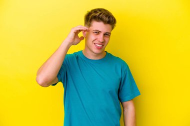 Sarı arka planda izole edilmiş genç beyaz bir adam bir şeye gülüyor, ağızlarını ellerle kapatıyor..