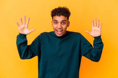 Genç Afro-Amerikalı kıvırcık adam, mor üzerine izole edilmiş. Hoş bir sürpriz alıyor, heyecanlı ve el kaldırıyor..