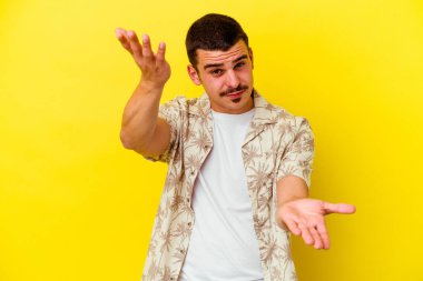 Sarı arka planda izole genç beyaz adam kollarıyla ölçek yapar, mutlu ve kendinden emin hisseder..