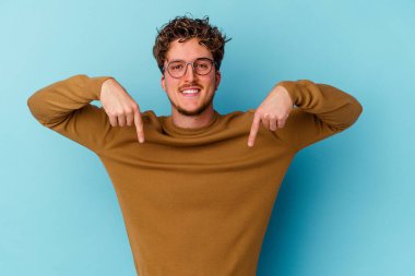 Gözlük takan genç beyaz adam mavi arka planda izole edilmiş, parmakları aşağıda, olumlu hisler içinde..