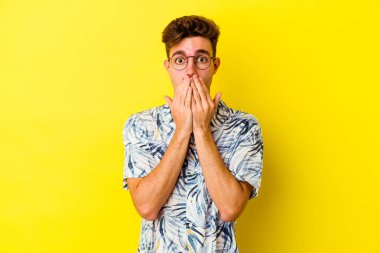 Sarı arka planda izole edilmiş genç beyaz adam şok olmuş, ağzı ellerle kaplanmış, yeni bir şey keşfetmeye hevesli..