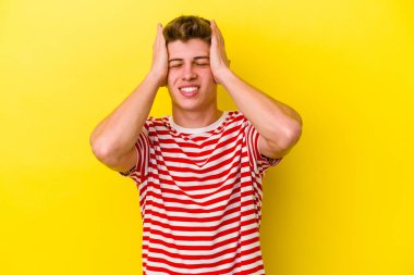 Sarı arka planda izole edilmiş genç beyaz adam ellerini başının üstünde tutarak neşe içinde gülüyor. Mutluluk kavramı.