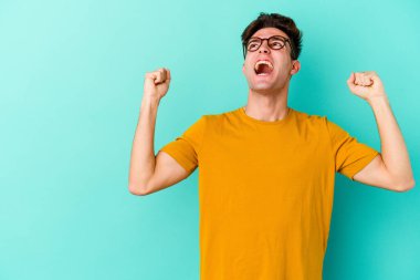 Mavi arka planda izole edilmiş genç beyaz bir adam zaferden sonra yumruğunu kaldırıyor, kazanan konsept..