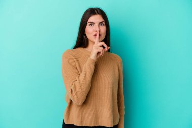 Mavi arka planda izole edilmiş genç beyaz kadın ya sır saklıyor ya da sessizlik istiyor..