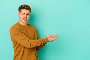 Mavi arka planda izole edilmiş genç beyaz bir adam palmiyesinde bir kopya alanı tutuyor..