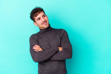 Kafkasyalı genç adam mavi arka planda izole edilmiş hedeflerine ve amaçlarına ulaşma hayali kuruyor.