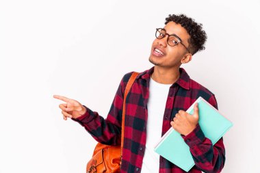 Genç Afro-Amerikalı kıvırcık erkek izole edilmiş, elinde kitaplarla gülümseyen ve işaret eden boş uzayda bir şey gösteriyor..