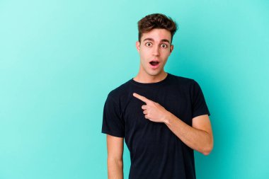 Mavi arka planda izole edilmiş genç beyaz adam yan tarafı işaret ediyor.