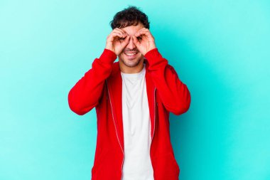 Mavi arka planda izole edilmiş genç beyaz adam gözlerinde sorun olmadığını gösteriyor.