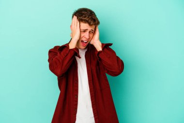 Kafkasyalı genç adam mavi arka planda izole edilmiş kulakları kulaklarıyla kapatıyor çok fazla ses duymamaya çalışıyor..