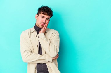 Mavi arka planda izole edilmiş, üzgün ve dalgın hisseden, kopyalama alanına bakan genç beyaz bir adam..