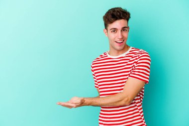 Mavi arka planda izole edilmiş genç beyaz bir adam palmiyesinde bir kopya alanı tutuyor..