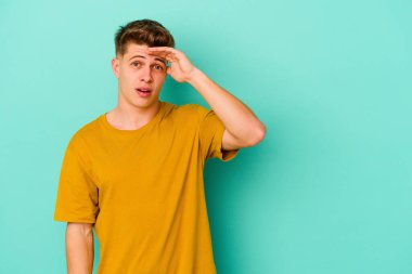Mavi arka planda izole edilmiş genç beyaz adam yüksek sesle bağırıyor, gözleri açık ve elleri gergin tutuyor..