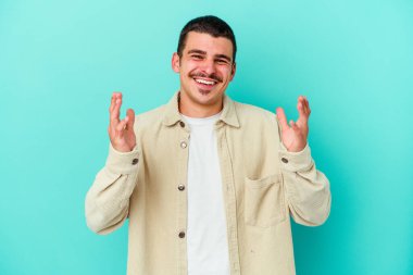 Kafkasyalı genç adam mavi arka planda izole edilmiş neşeli bir şekilde gülüyor. Mutluluk kavramı.