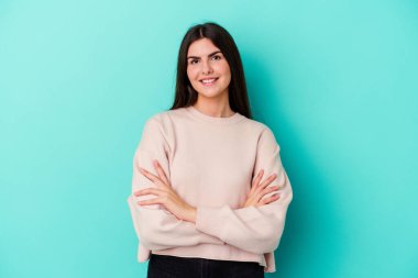 Mavi arka planda izole edilmiş genç beyaz kadın kendini güvende hissediyor, kararlılıkla kollarını kavuşturuyor..