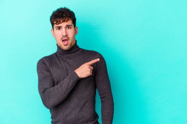 Mavi arka planda izole edilmiş genç beyaz adam yan tarafı işaret ediyor.