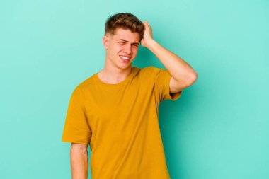 Kafkasyalı genç adam mavi arka planda izole edilmiş bir şekilde bir şeyi unutuyor. Alnına avuç içi ve gözlerini kapayarak vuruyor..