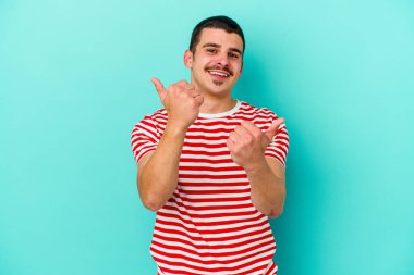 Kafkasyalı genç adam mavi arka planda izole edilmiş. Baş parmağını kaldırıyor, gülümsüyor ve kendinden emin..
