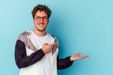 Mavi arka planda izole edilmiş gözlüklü genç beyaz adam palmiye üzerinde bir fotokopi alanı tutuyor..