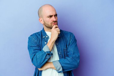 Kafkasyalı genç kel adam mor arka planda izole edilmiş düşünüyor ve yukarı bakıyor, yansıtıyor, düşünüyor, hayal kuruyor..