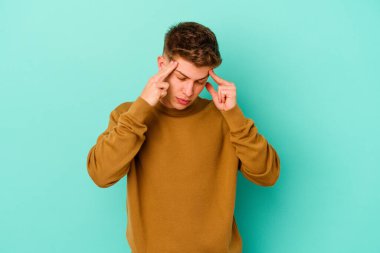 Genç beyaz adam mavi arka planda izole edilmiş tapınaklara dokunuyor ve başı ağrıyor..