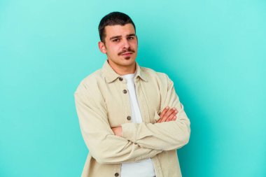 Kafkasyalı genç adam mavi arka planda izole edilmiş şüpheli, belirsiz, seni muayene ediyor..