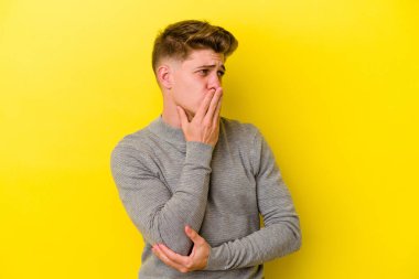 Sarı arka planda izole edilmiş genç beyaz adam esniyor. Ağzı eliyle kapatan yorgun bir hareket sergiliyor..