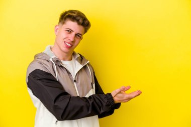 Sarı arka planda izole edilmiş genç beyaz bir adam palmiyesinde bir kopya alanı tutuyor..